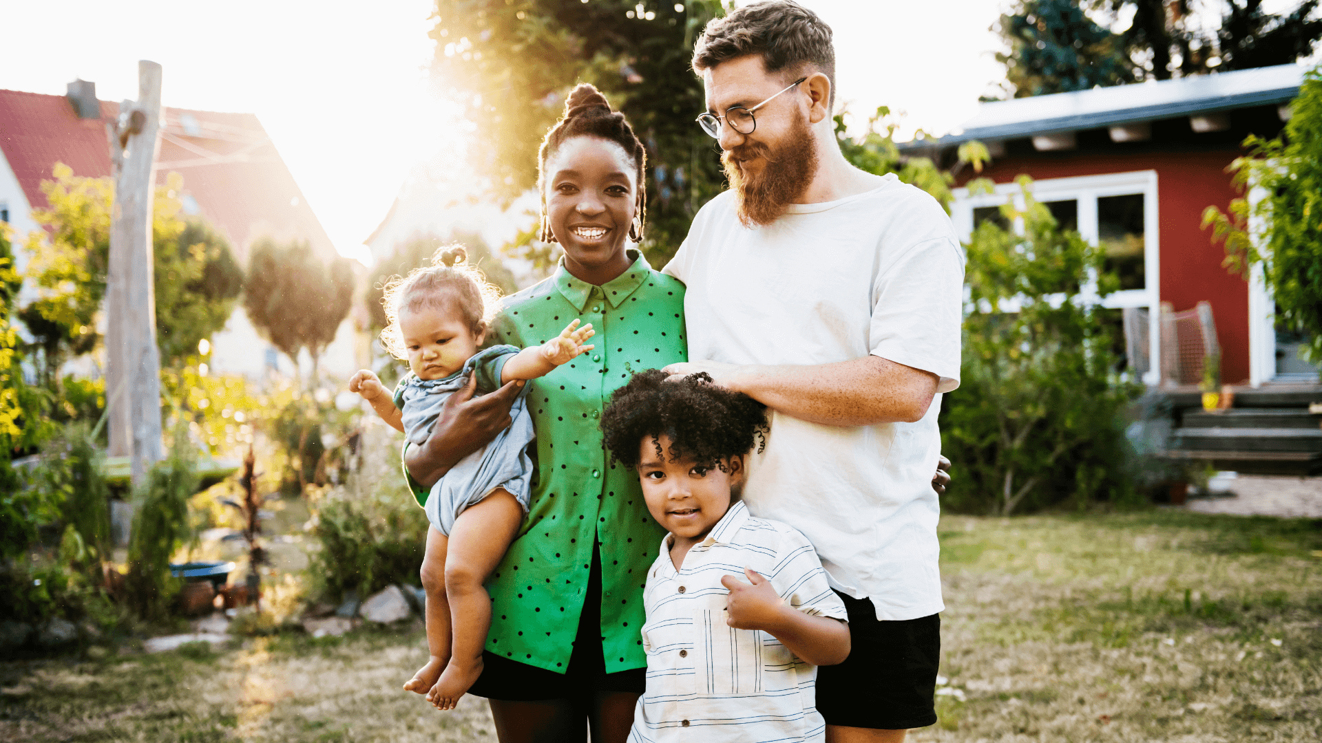 Mother, father and their two children stand outside their home, smiling.