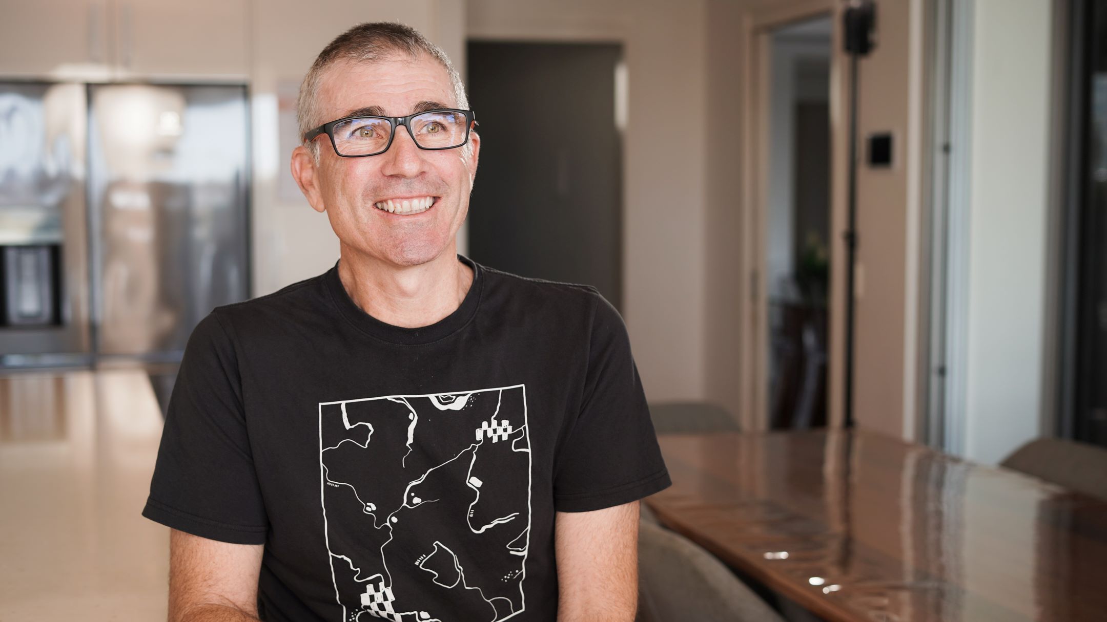 A male claimant sits in his kitchen, smiling at camera to share his experience with Acenda